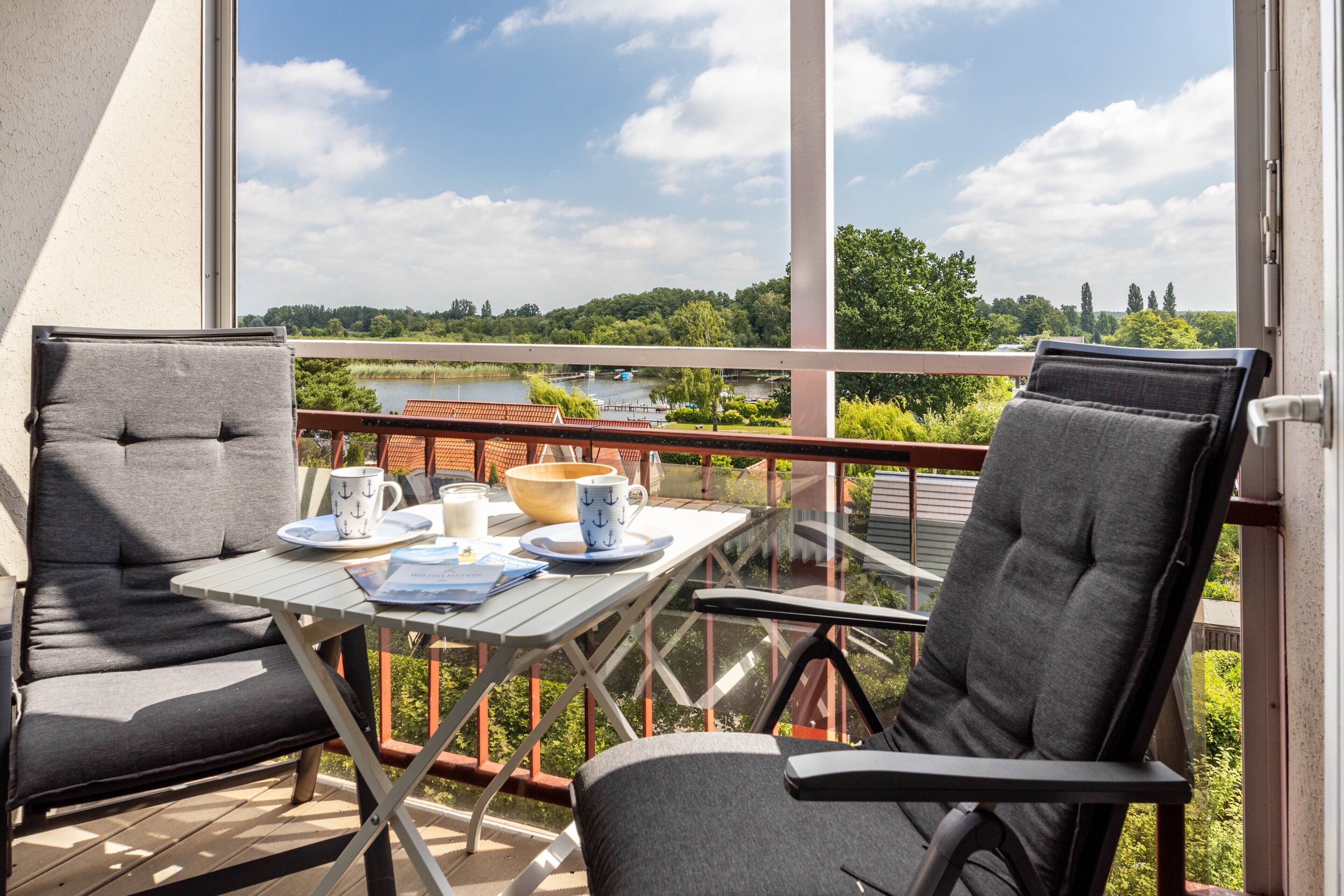 A balcony with two chairs, a table with a bowl, cups, and a book.