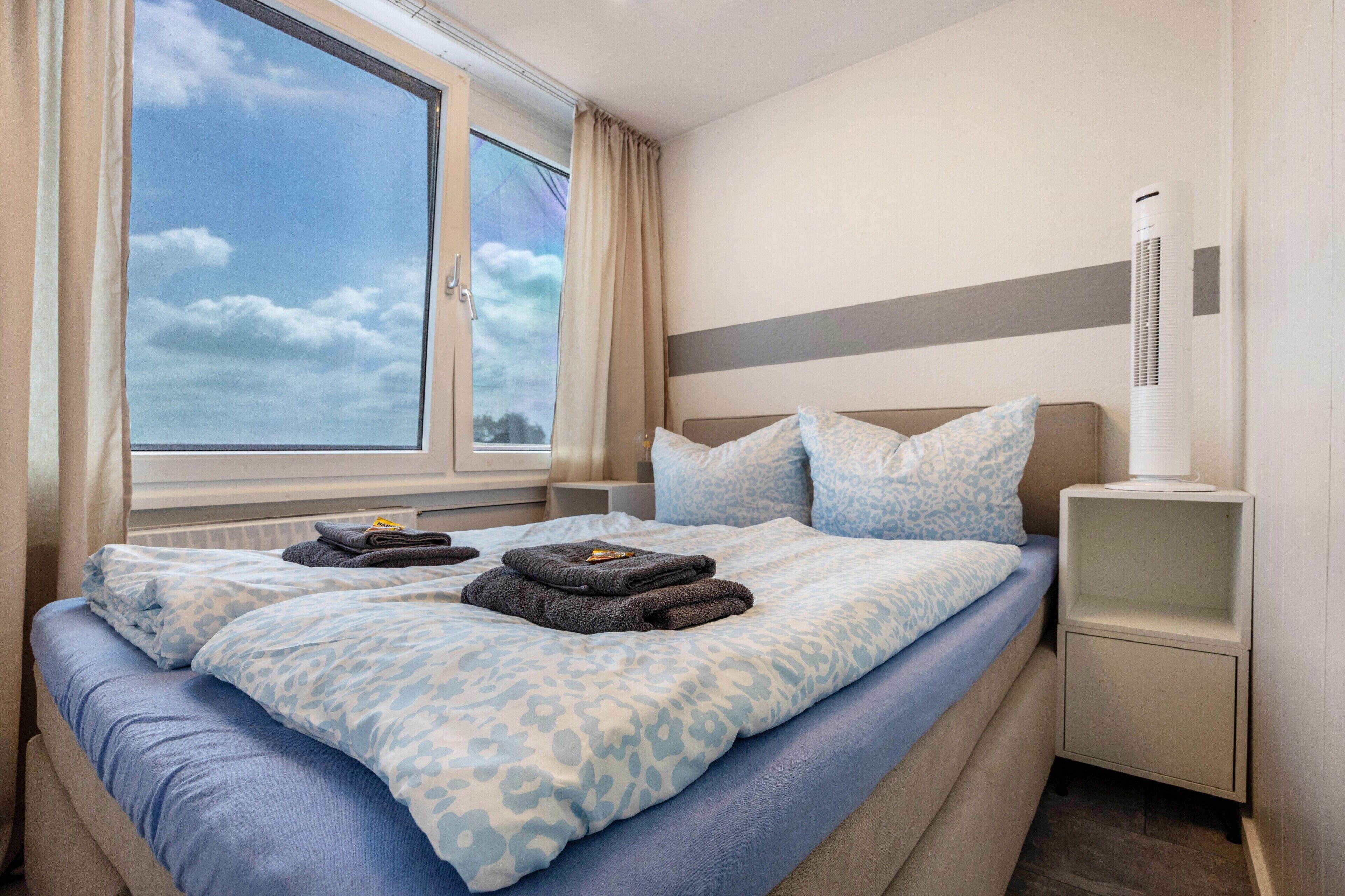 A hotel room with a bed, a window, a bedside table, and an air conditioning unit.