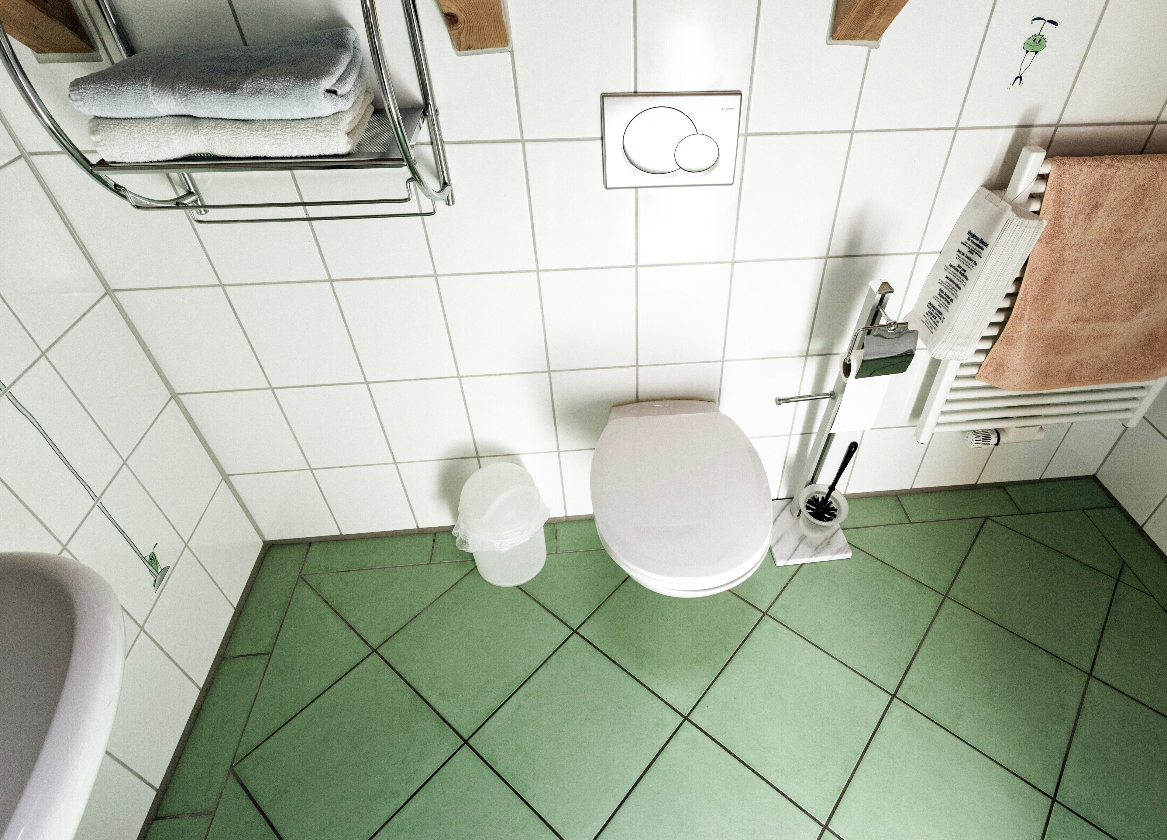 A bathroom with a toilet, a sink, a towel rack with folded towels, and a toilet brush.