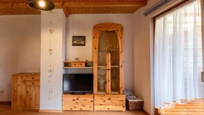 Ein Zimmer mit Holzmöbeln, einem Fernseher, einem Holzschrank und einem fenster mit Vorhängen.