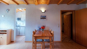 Ein Holzespeisetisch mit Stühlen, eine Wandleuchte und Blick in eine Küche.