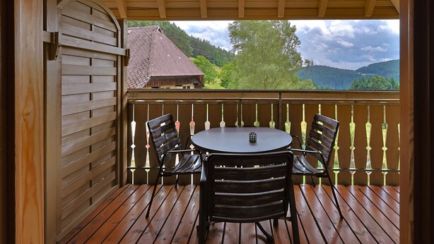Eine Holzterrasse mit einem runden Tisch und vier Stühlen, mit Blick auf eine gebirgige Landschaft.