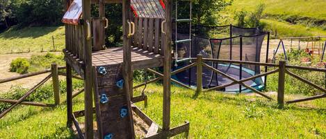 A wooden play structure with a climbing wall and a trampoline.