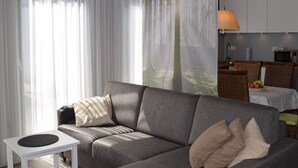 Ett modernt vardagsrum med en grå soffa, ett vitt sidobord och ett köksområde i bakgrunden.