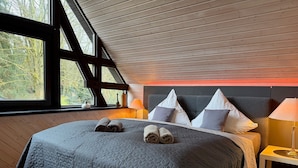 Een slaapkamer met een groot bed, een houten plafond en een raam met uitzicht op bomen.