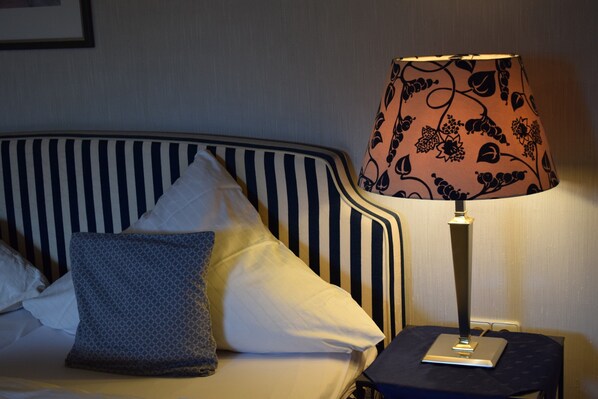 A bed with striped headboard, two pillows, a bedside table with a lamp, and a framed picture on the wall.