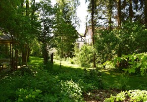 A lush garden with a gazebo, dense trees, and a building in the background.