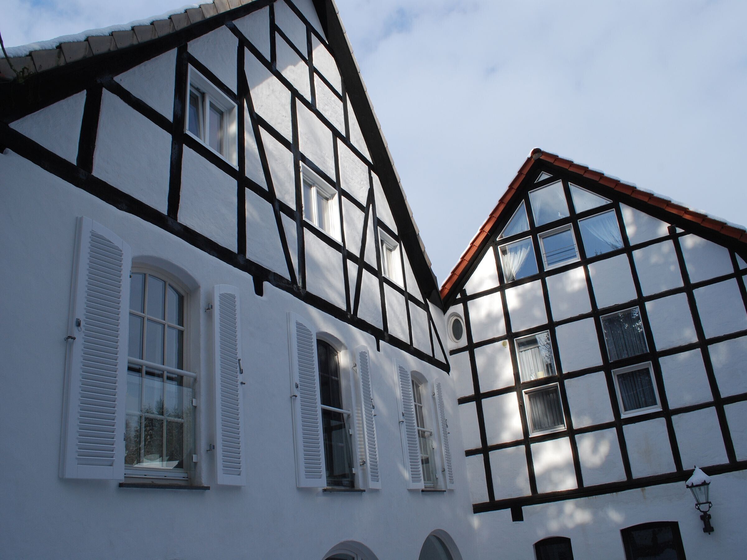 A traditional half-timbered building with multiple windows and shutters, a pitched roof, and a visible chimney.