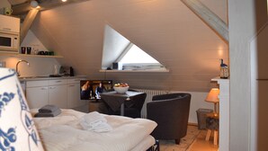 Un dormitorio con cama, escritorio, silla, microondas, una mesita y una ventana.