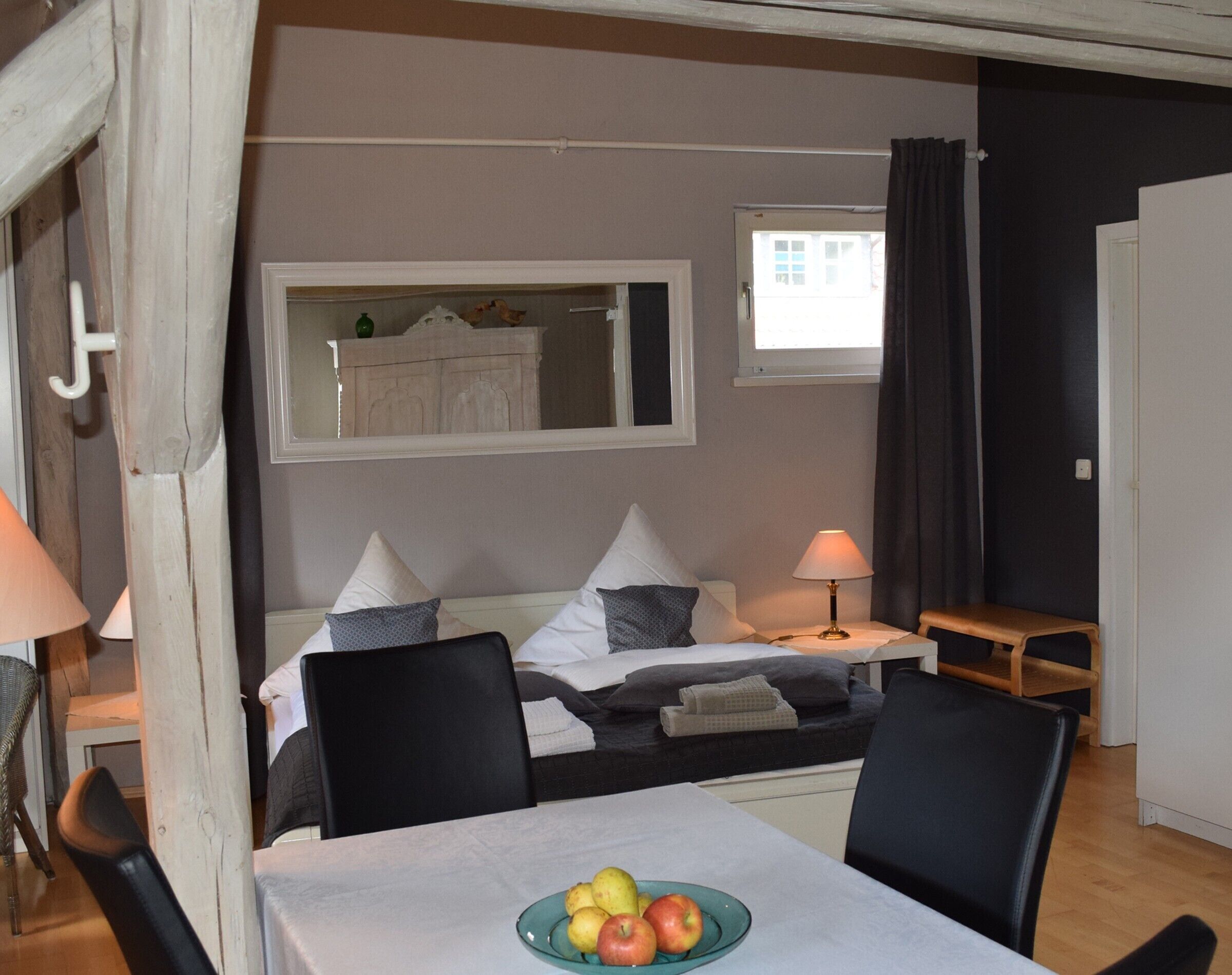 Un dormitorio con cama, mesita de noche, lámpara y una mesa con fruta.