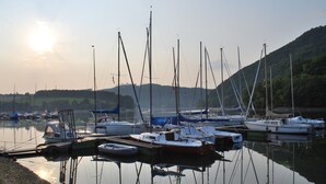 A marina with multiple boats docked, calm water, and a hilly landscape in the background. - Country House Bornemann Apartment 6 (Diemelsee)