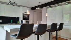 A modern kitchen with a central island, bar stools, pendant lighting, and built-in appliances. - Landhaus Bornemann Holiday Apartment 7 (Diemelsee)