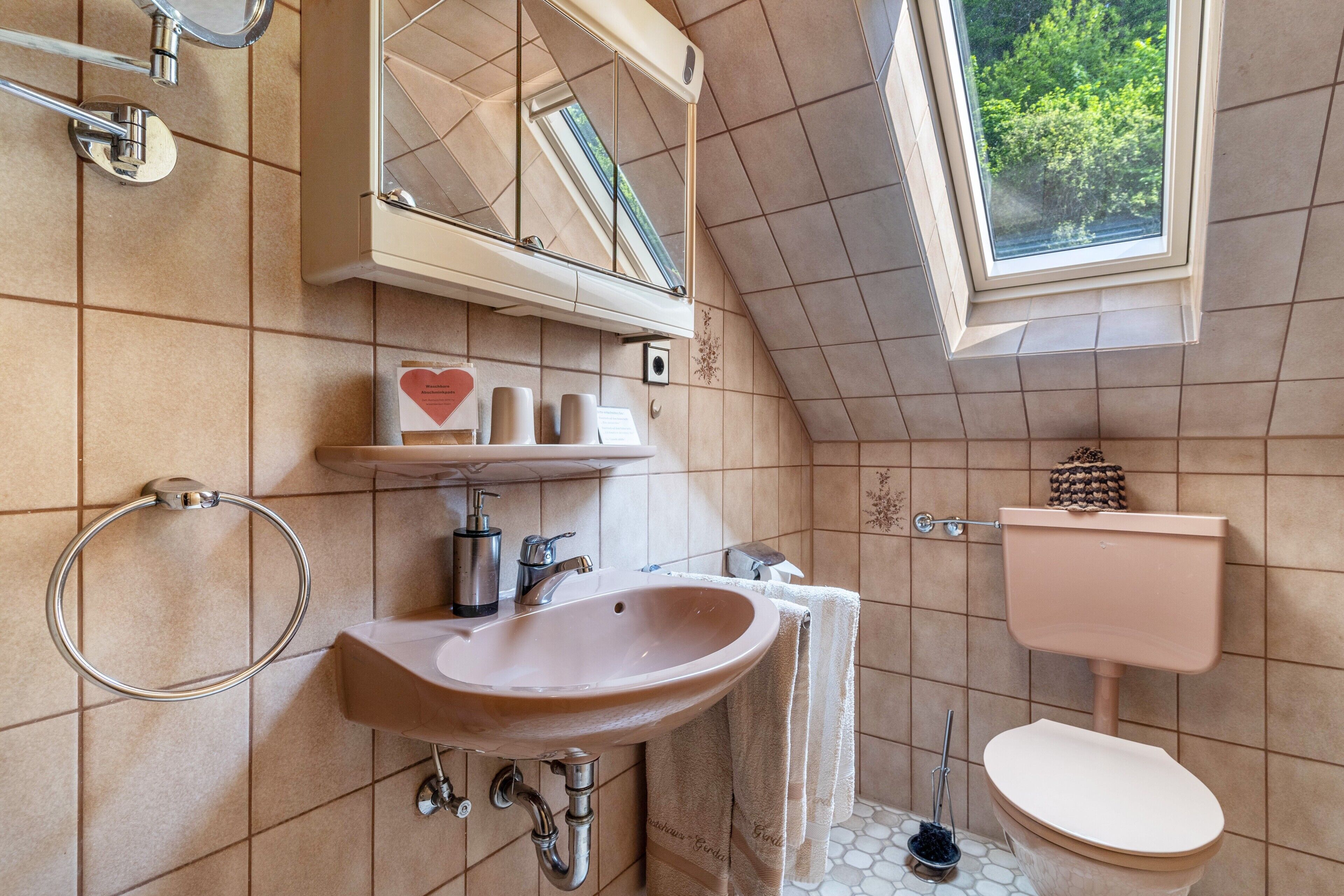 A bathroom with a skylight, a sink, a toilet, and a mirror.