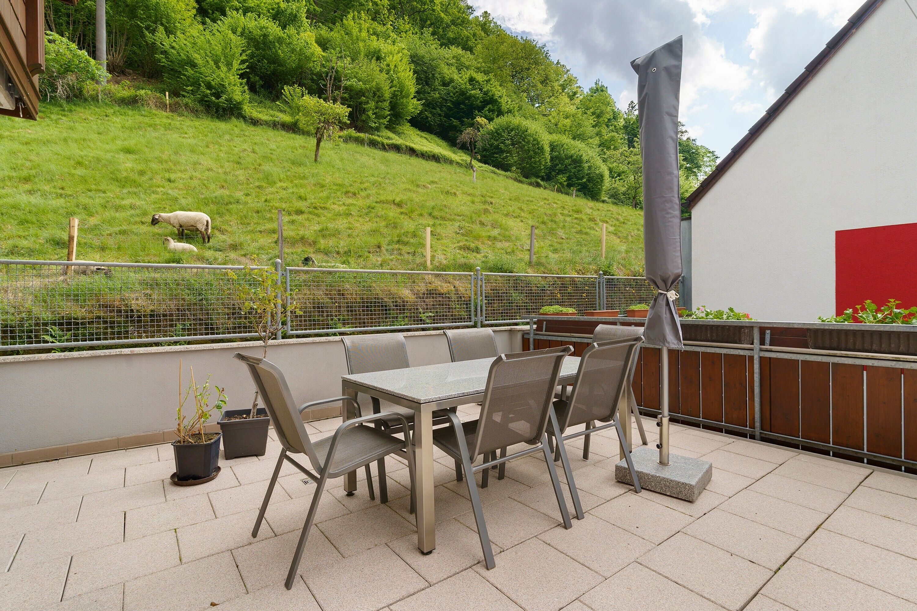 Une terrasse avec une table et des chaises, une clôture et une vue sur une colline verdoyante.