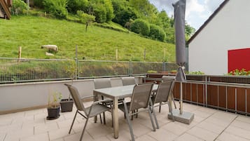 Une terrasse avec une table et des chaises, une clôture et une vue sur une colline verdoyante.