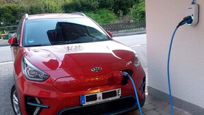 Een rode auto geparkeerd bij een oplaadstation, met een blauwe kabel aangesloten.