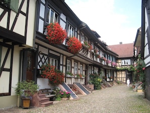 Ein traditionelles Fachwerkhäuschen mit einem Kopfsteinpflasterhof, Holzbanken und Blumenkästen an den Fensterbänken.