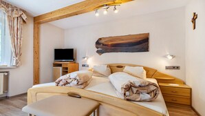 Een slaapkamer met een houten plafond, een bed met kussens, een nachtkastje, een televisie en een kunstwerk aan de muur.