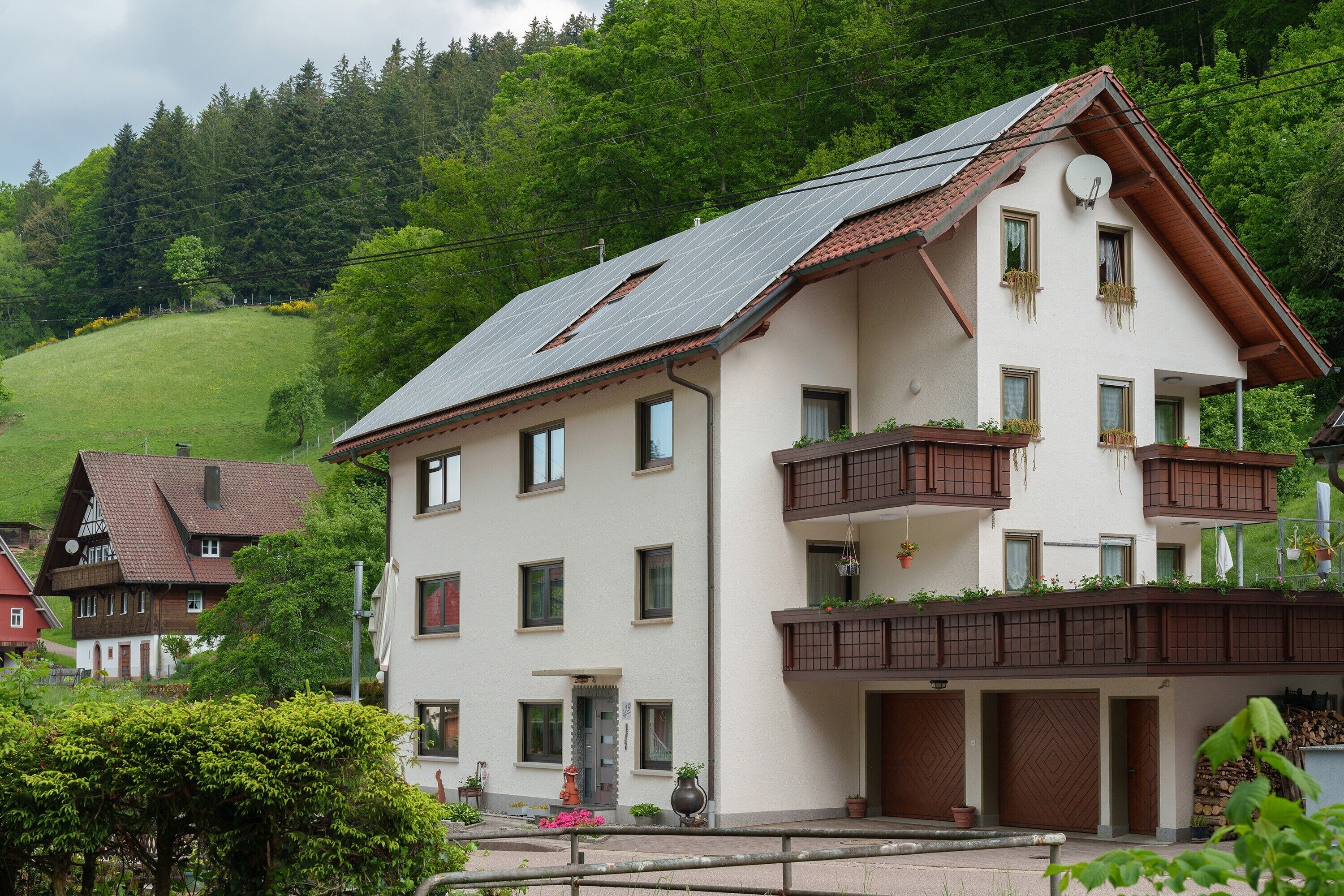 Ein zweistöckiges Gebäude mit geneigtem Dach, mehreren Fenstern und einem Balkon mit Pflanzen.