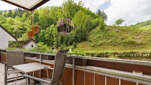 Een balkon met een tafel en stoelen, met uitzicht op een weelderig groen landschap met bomen en heuvels.