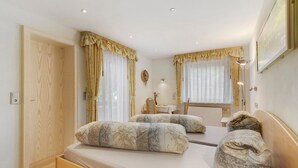 Een slaapkamer met twee bedden, een houten garderobe, een spiegel, een tafel met stoelen en een raam met gordijnen.
