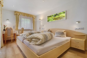 Une chambre à coucher comprenant un lit, une table de chevet, une chaise, un bureau, une lampe et un tableau accroché au mur.