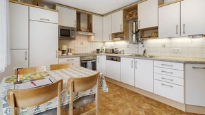 Een keuken met witte kasten, een magnetron, een fornuis en een eettafel met stoelen.