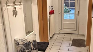Un corridoio con una porta, un appendiabiti, una piccola mensola con oggetti decorativi e un cuscino decorato.