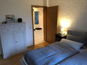 A bedroom with a bed, a nightstand, a dresser, and a door leading to a bathroom. - Apartment 'Fleckenberg' with Mountain View, Private Terrace and Wi-Fi (Schmallenberg OT Fleckenberg)