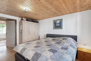 A bedroom with a wooden ceiling, a bed with a quilt, a nightstand, a wooden wardrobe, and a framed picture on the wall.