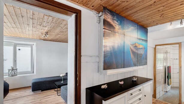 Una habitación con techo de madera, un cuadro grande de un barco, una encimera negra y vistas a un balcón.