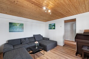 A modern living room with a grey sectional sofa, a small black table with a vase, wooden flooring, and a ceiling with exposed beams.