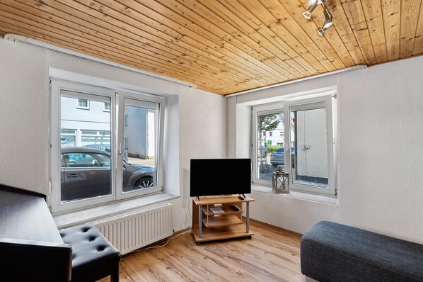 A room with a wooden ceiling, large windows, a flat-screen TV on a stand, a bench, and a radiator.