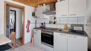 Una cocina moderna con armarios blancos, horno de acero inoxidable, microondas y techo de madera.