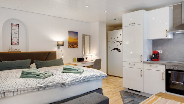 A modern bedroom with a bed, bedside table, lamp, and a view into the kitchen area. - Studio 'Gelis' with Mountain View, Private Terrace and Wi-Fi (Ihringen)