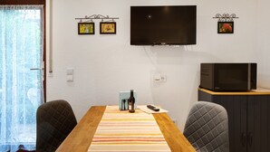 A dining area with a wooden table, two chairs, a TV, a microwave, and a window with curtains. - Studio 'Gelis' with Mountain View, Private Terrace and Wi-Fi (Ihringen)