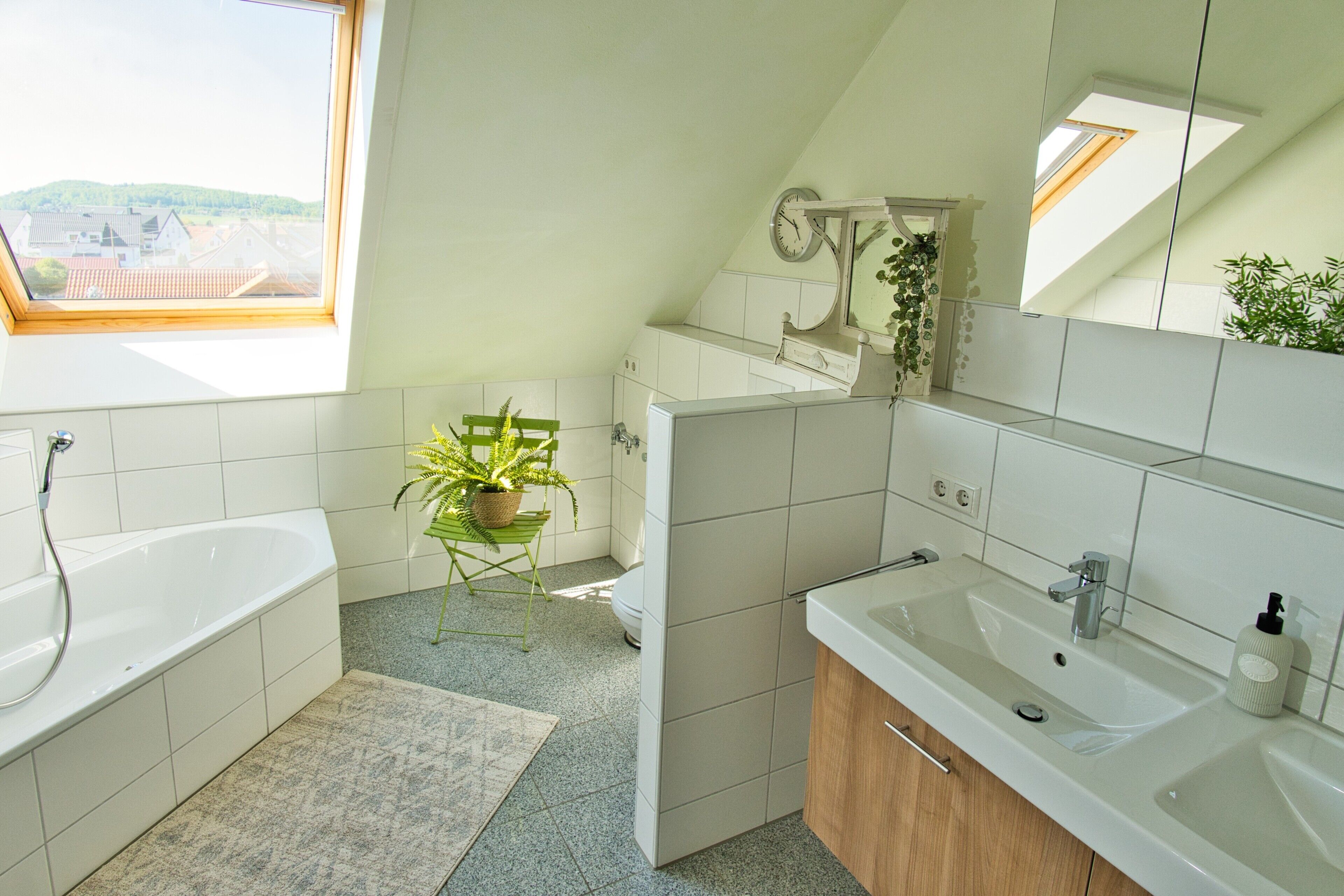 Un bany modern amb una finestra panoràmica, una banyera, un lavabo i una planta en test.