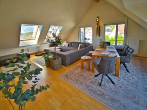 Un espacio tipo loft con sofá, mesa de comedor, sillas, ventanas amplias y una planta.
