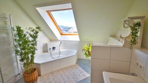 Un baño moderno con tragaluz, una bañera independiente, un espejo grande y una planta en maceta.