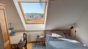 Un dormitorio con techo inclinado, una cama, una silla, una mesita y un radiador.
