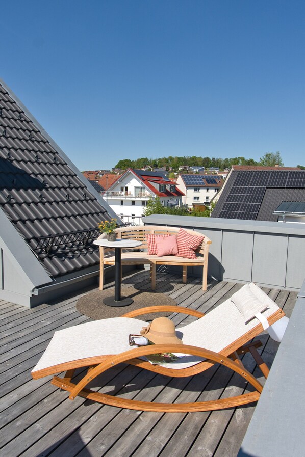 Una terraza en la azotea con una mesa de madera, dos sillones de relax y vistas de los edificios circundantes.