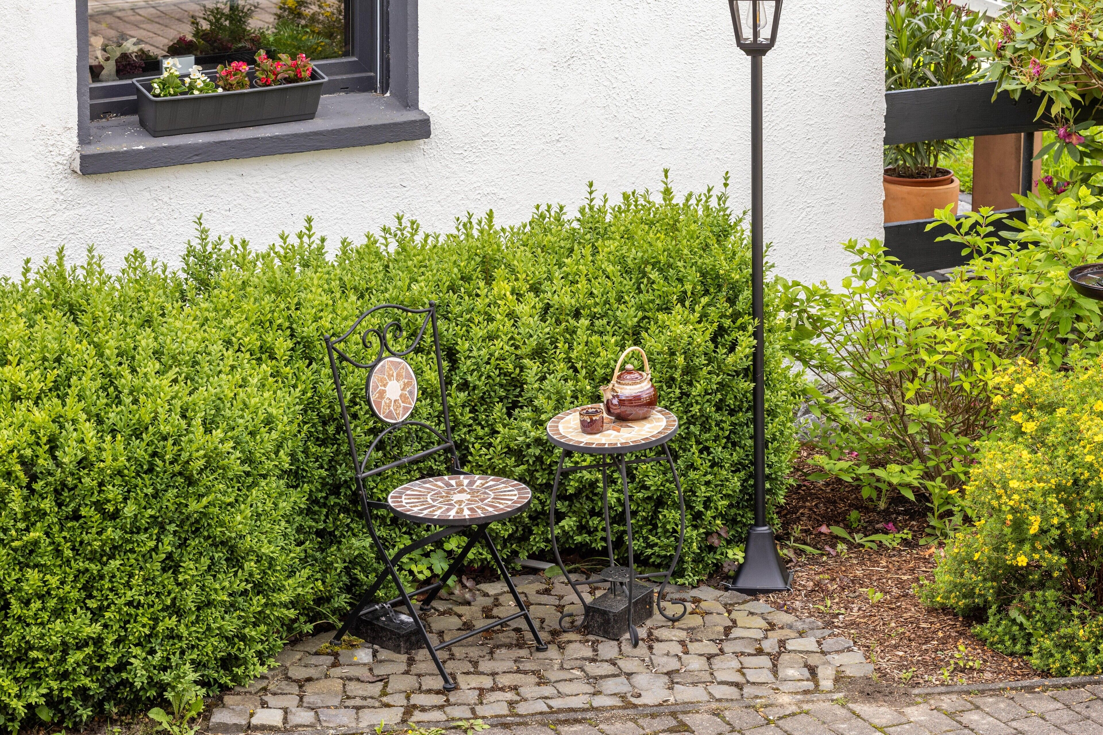 Eine Terrasse mit einem kleinen Tisch und Stuhl, einem Blumentopf und einem Fenster mit Blumen.