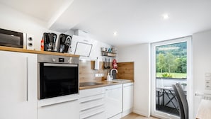 Eine moderne Küche mit weißen Schränken, einem eingebauten Ofen, einer Kaffeemaschine und Blick auf einen Balkon mit Tisch und Stühlen.
