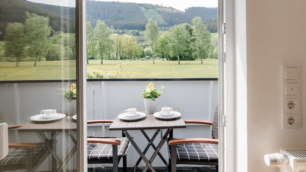 Ein Balkon mit Tisch für zwei Personen, Stühlen und Blick auf eine grüne Landschaft.