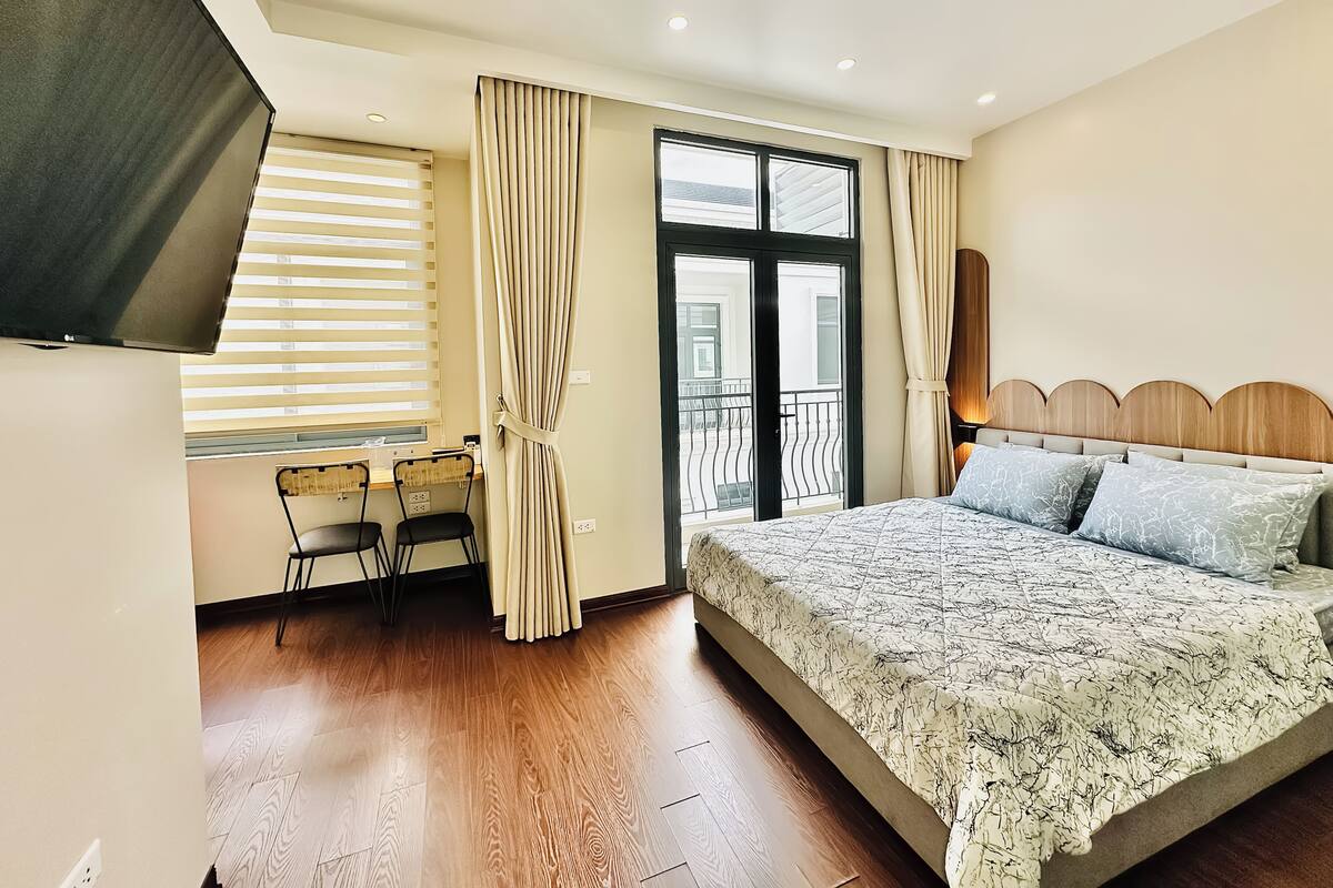 Ein Schlafzimmer mit Bett, Schreibtisch mit Stühlen, Fernseher und Balkon.