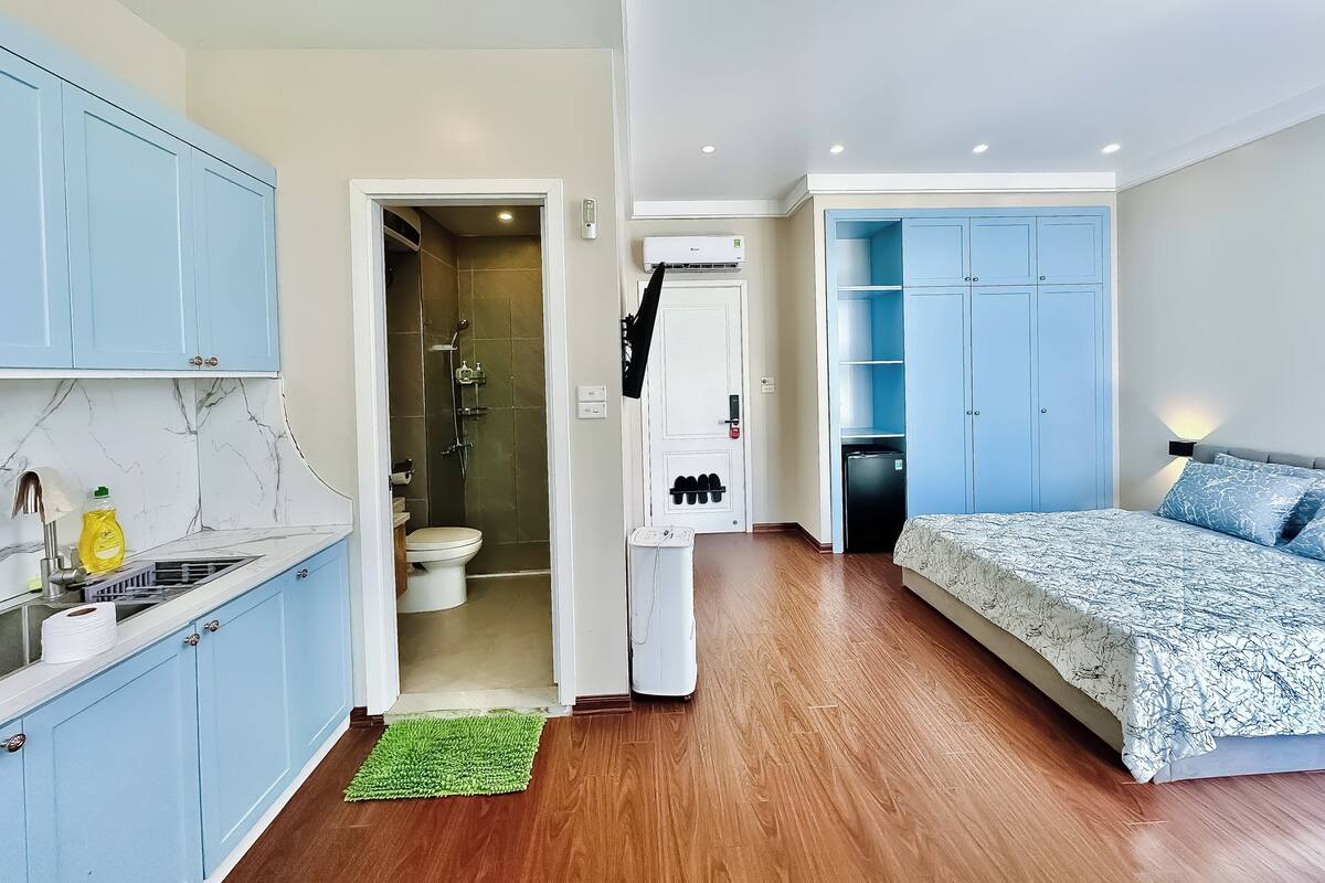 Ein kleines Hotelzimmer mit einer Küchenzeile, einem Badezimmer mit Dusche und einem Bett mit geblümter Bettwäsche.