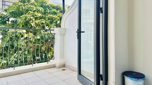 A balcony with a metal railing, a glass door, and a trash bin. - Anvi House - Vinhomes Marina (Hai Phong)