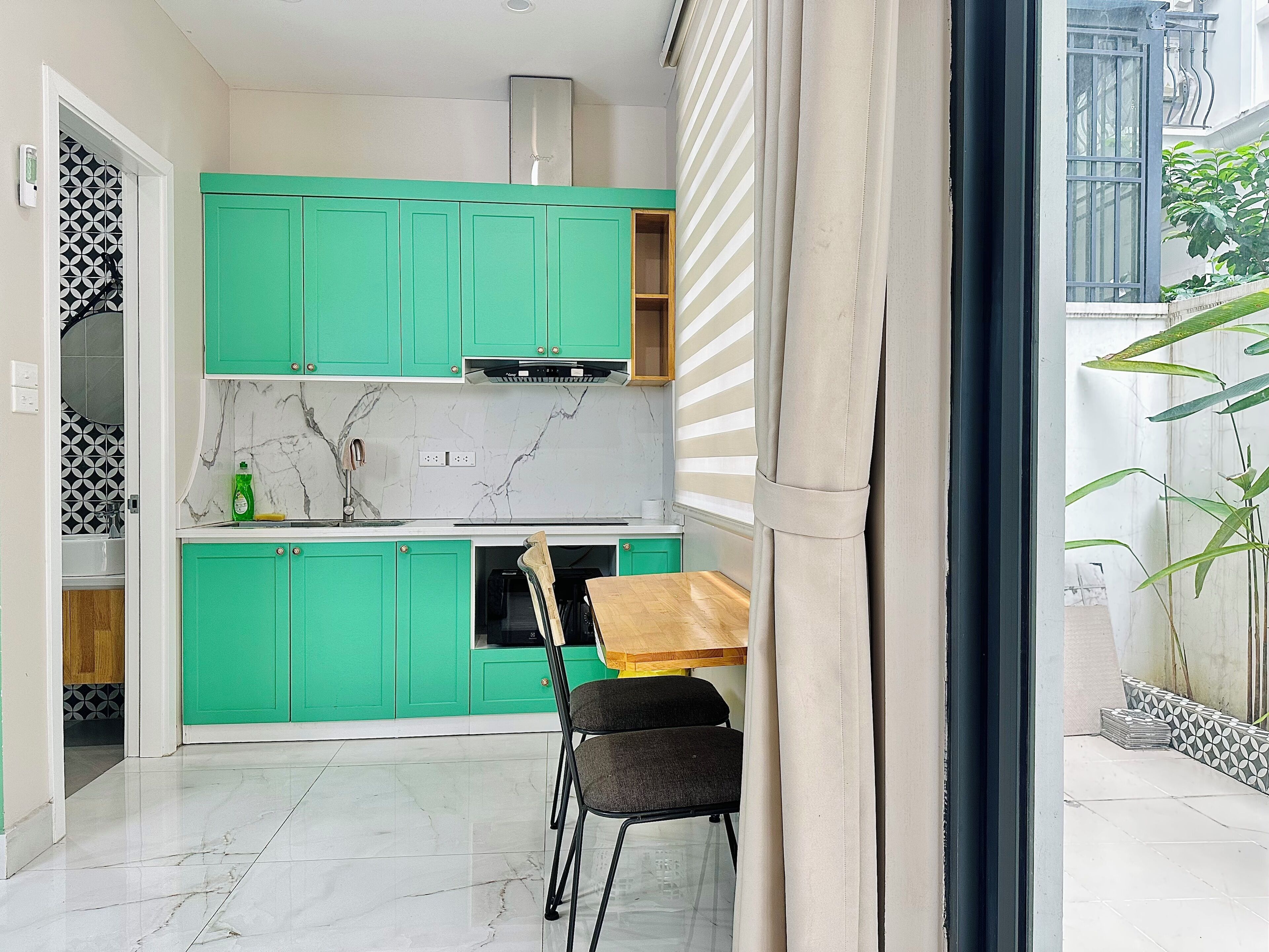 Una cocina compacta con gabinetes verdes, una encimera de mármol y un comedor con mesa y sillas.