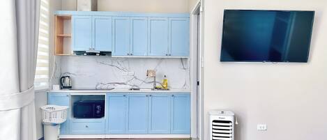 A compact kitchen with light blue cabinets, a marble backsplash, a built-in oven, and a Kangaroo portable air conditioner.