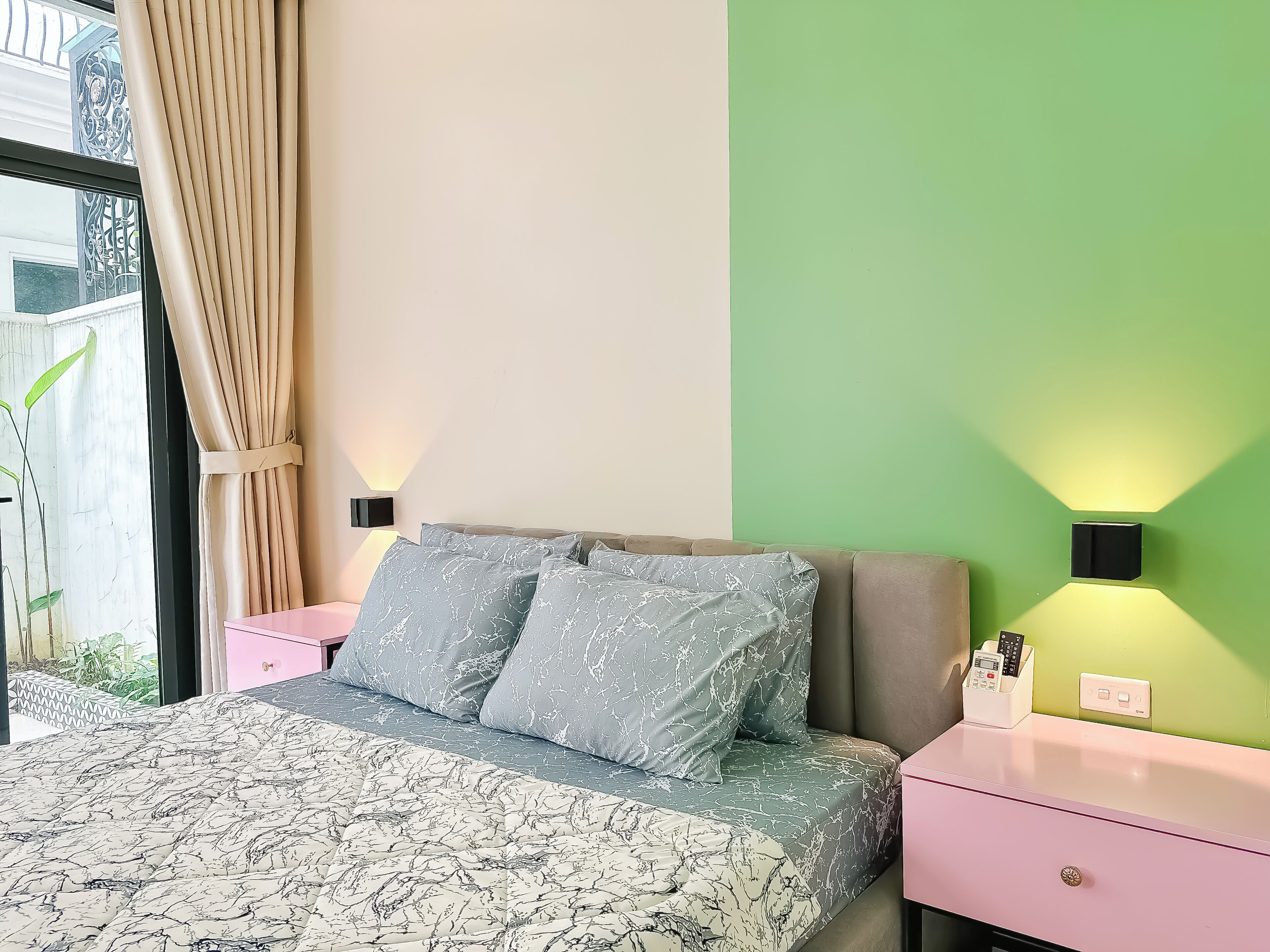 A bedroom with a bed, nightstands, a green wall, and a window with curtains.